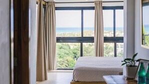 Un dormitorio con un ventanal grande, una cama, un aparador de madera y vistas al exterior.