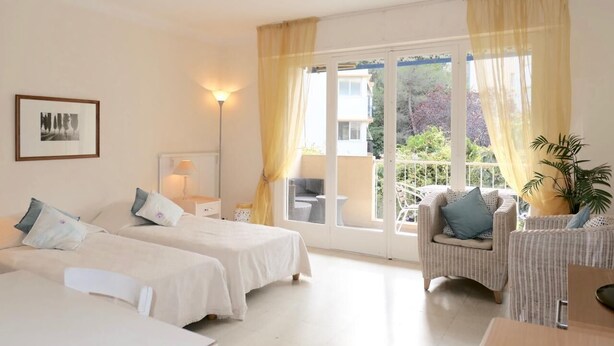 Habitación de hotel con dos camas, un balcón con una silla y una mesa, y un ventanal grande con cortinas.