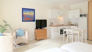 Un espacio habitable compacto con kitchenette, televisor, comedor y una cama individual.