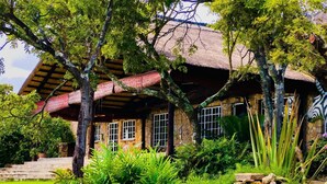 Una casa rústica con techo de paja, muros de piedra y un jardín cuidado con diversas plantas y un muro de piedra.