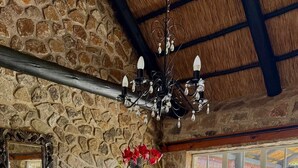 Una habitación de paredes de piedra con una mesa de vidrio rodeada de sillas, una araña y un ventanal con vistas a follaje.