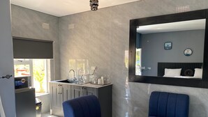 A modern hotel room with a kitchenette, two blue armchairs, a small wooden table, and a large mirror. - Executive studio apartment near the airport - 2320 (Harare)