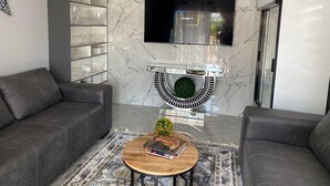 A modern living room with a grey sofa, a coffee table with a book, a TV mounted on the wall, and a decorative circular shelf.