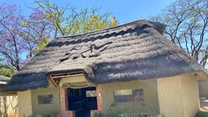 Edificio con techo de paja y entrada de ladrillo, rodeado de follaje y árboles.