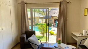 Habitación de hotel con cama, escritorio, silla y vistas a la piscina y al jardín.