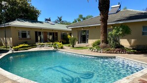 Una piscina con borde de azulejos, rodeada de baldosas de piedra y un pequeño jardín con plantas y una palmera.