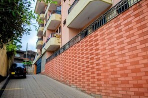 Eine schmale Straße mit einer roten Backsteingemäuer auf einer Seite und einem mehrstöckigen Gebäude mit Balkonen auf der anderen.
