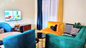 Ein Wohnzimmer mit einer Couch, Sesseln, einem Couchtisch, einem Fernseher und einem Schrank.