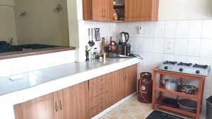Een keuken met houten kastjes, een gasfornuis, een gasfles en een waterkoker.