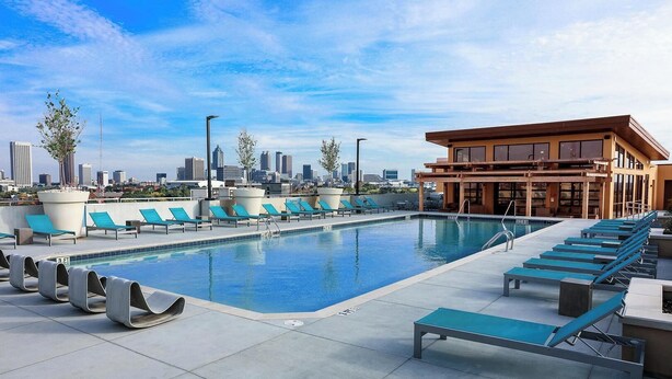 A rooftop pool with lounge chairs and a city skyline view. - Landing | Incredible 1BD, Clubhouse, Gym (Atlanta)