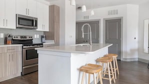 A modern kitchen with stainless steel appliances, a central island with bar stools, and a grey door in the background. - Landing | Incredible 1BD, Clubhouse, Gym (Atlanta)