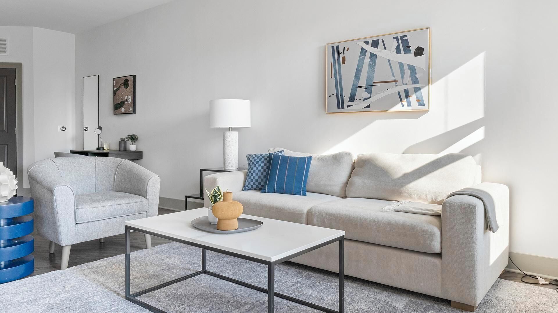 Un salon moderne avec un canapé gris, une table basse blanche et un coussin bleu à motifs.