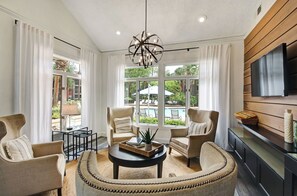 Una sala de estar moderna con vista a la piscina, que incluye una mesa redonda, dos sillones, un sofá y un televisor montado en la pared.