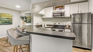 Uma cozinha moderna com ilha central, eletrodomésticos de aço inoxidável e área de jantar com banquetas.