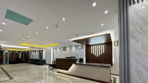 Een moderne hotel lobby met een marmeren receptiebalie, een zithoek en een schone, gepolijste vloer.