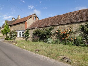 A stone building with a tiled roof, a window, and a garden with flowers. - Granary Cottage (Chippenham)