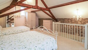 A bedroom with a sloped ceiling, a bed with floral bedding, a dresser, and a stone wall. - Granary Cottage (Chippenham)