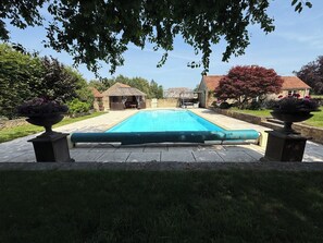 A rectangular swimming pool with a tiled deck, surrounded by grass and trees. - Granary Cottage (Chippenham)