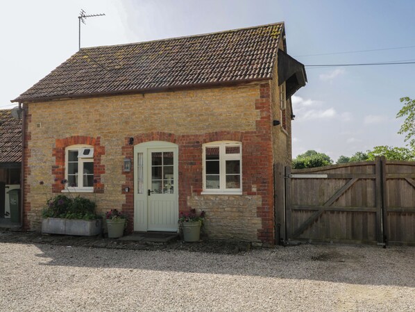A two-story stone house with a tiled roof, a white door, and a wooden fence. - Granary Cottage (Chippenham)