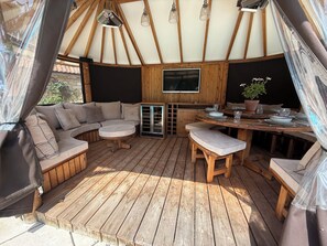A wooden deck with a sofa, round table, and benches. - Granary Cottage (Chippenham)