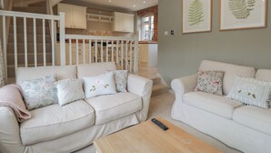 A spacious living room with two white sofas, a wooden coffee table, and a staircase leading to a kitchen. - Granary Cottage (Chippenham)