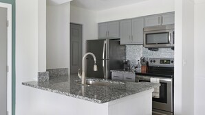 A modern kitchen with granite countertops, stainless steel appliances, and grey cabinetry. - Landing | Stunning 1BD, Courtyard, Pool (Nashville)