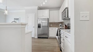 Une cuisine moderne avec des meubles blancs, des appareils électroménagers en acier inoxydable et un plancher en bois.