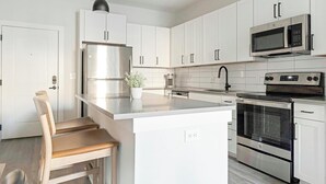 Una cocina moderna con armarios blancos, electrodomésticos de acero inoxidable, una isla central y un horno empotrado.