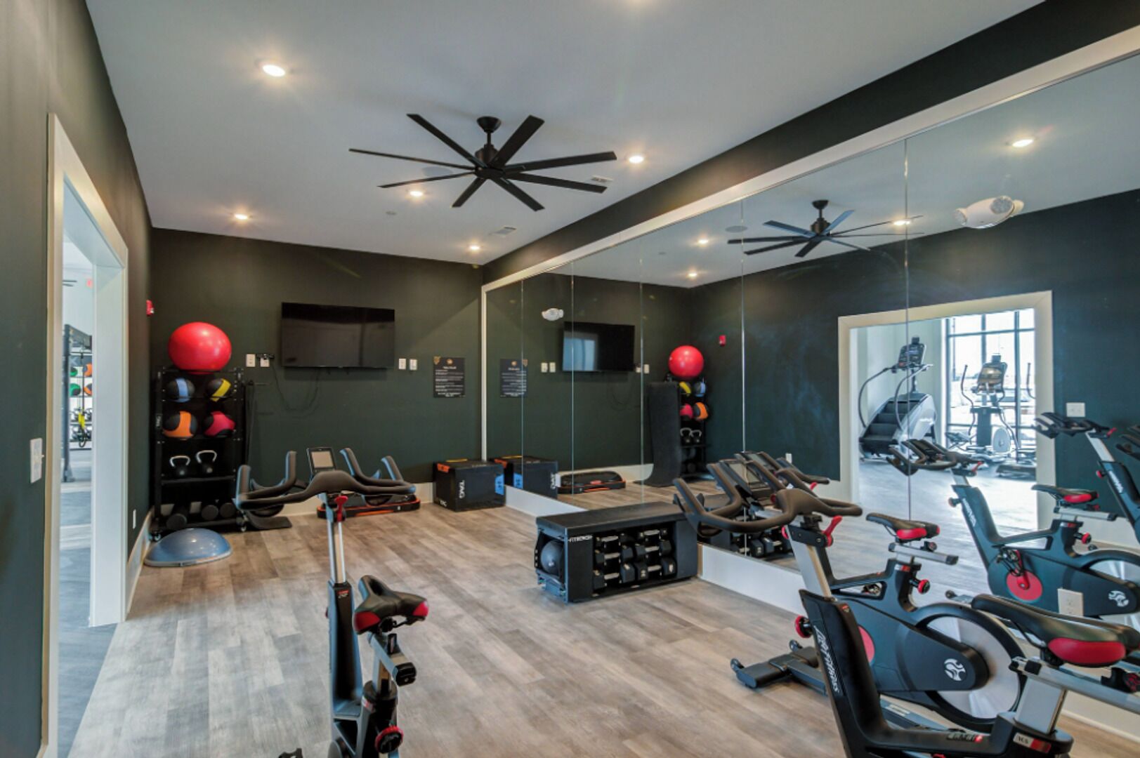 A modern gym with exercise equipment, a large mirror, and a ceiling fan.