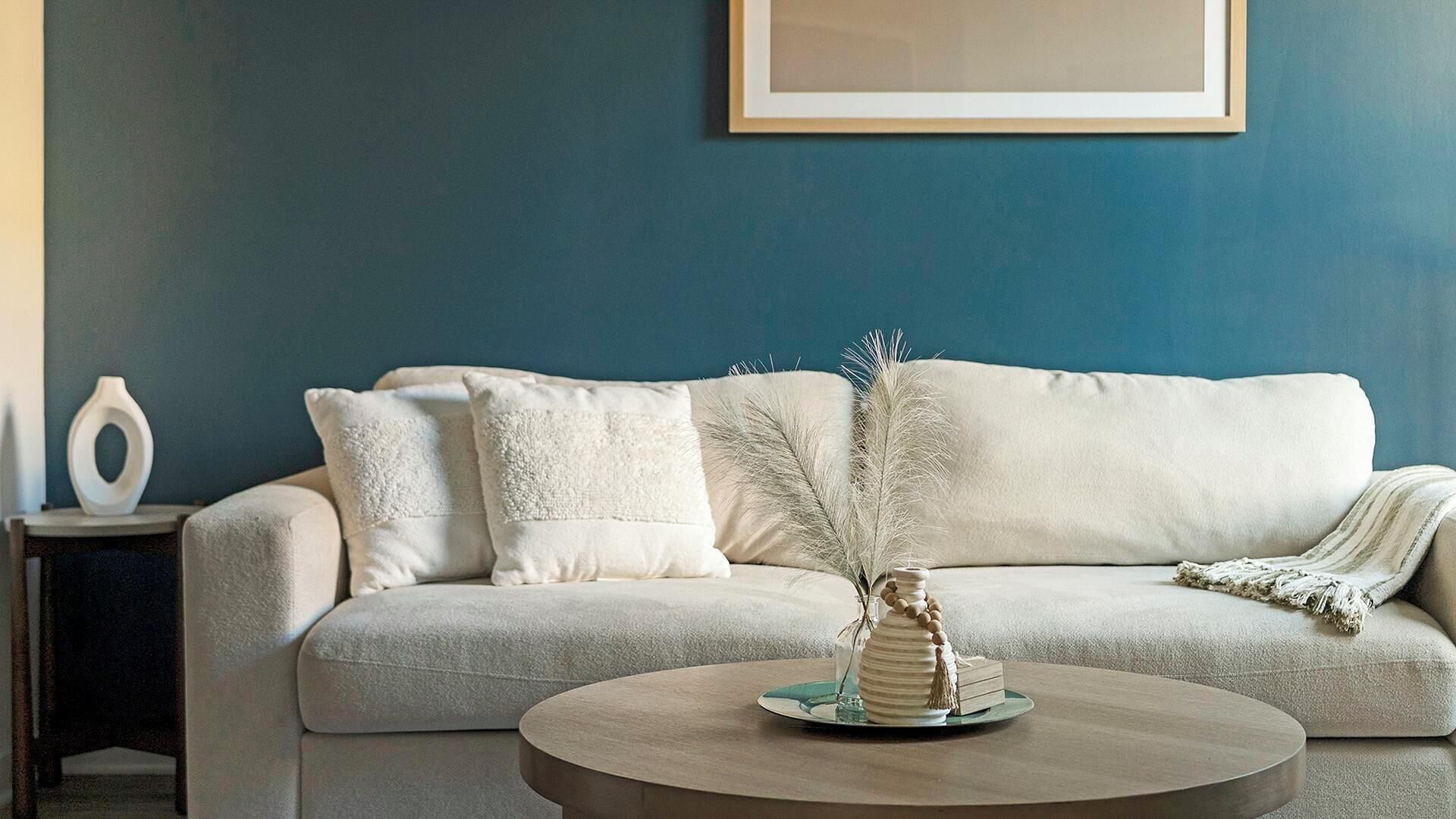 A living room with a sofa, a coffee table, and a vase with dried plants.