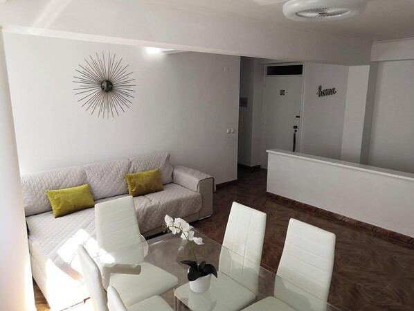 Ein modernes Wohnzimmer mit einer Couch, Sesseln, einem Glastisch und einer Wanddekoration.