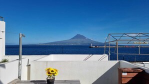 A balcony with a clear view of the sea, a mountain in the distance, and a metal structure.
