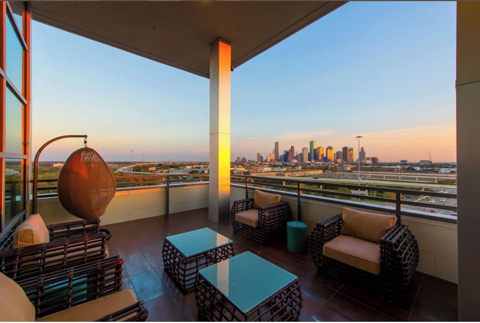 A balcony with wicker furniture, a glass table, and a view of a city skyline.