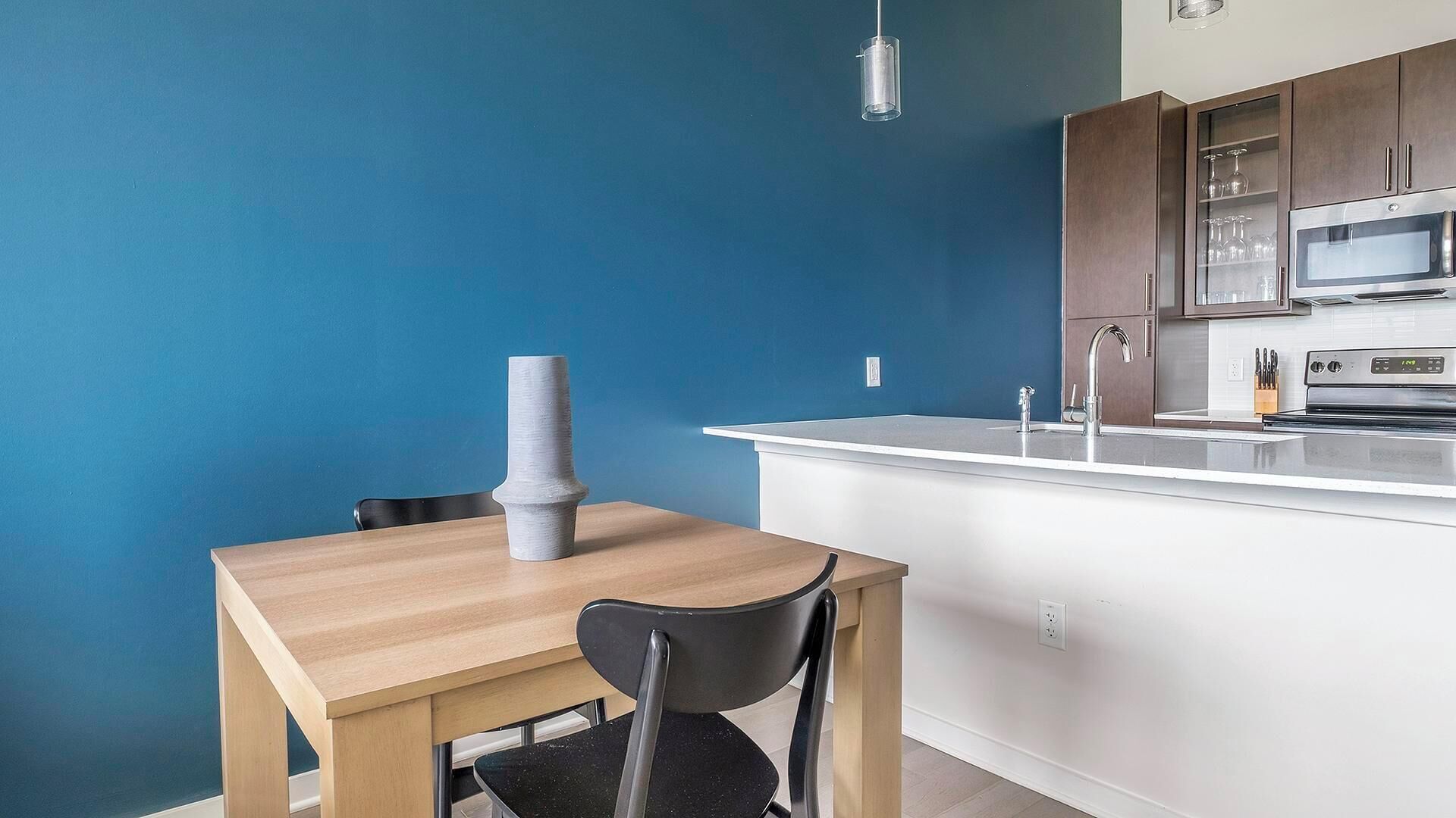 A modern kitchen with a blue accent wall, a wooden dining table, and a black chair.