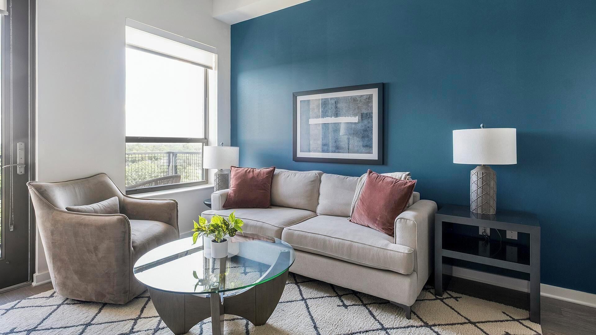 Een woonkamer met een beige bank, een glazen salontafel, een stoel en een blauwe accentmuur.