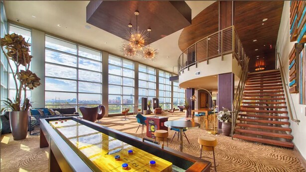 Een ruime lobby met een pooltafel, comfortabele zitplaatsen, grote ramen en een trap.