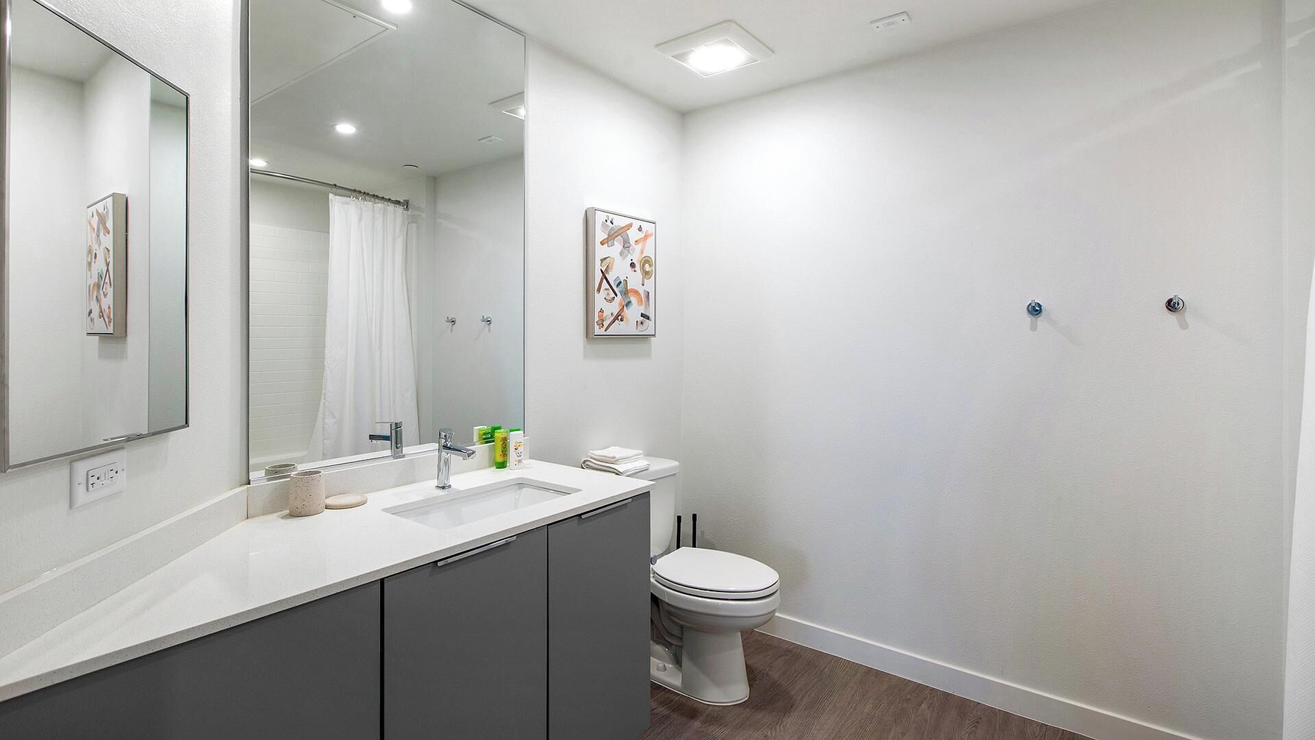 A modern bathroom with a large mirror, a sink, a toilet, and a shower curtain.