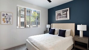 Ein Schlafzimmer mit einem Bett, zwei Nachttischen, einem Fenster und Kunstwerken an den Wänden.