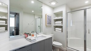 A modern bathroom with a large mirror, a shower, a toilet, and a vanity with toiletries. - Landing | Chic 2BD, Gym, Clubhouse (Spring Valley)