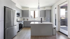A modern kitchen with stainless steel appliances, a central island, and a large window providing natural light.