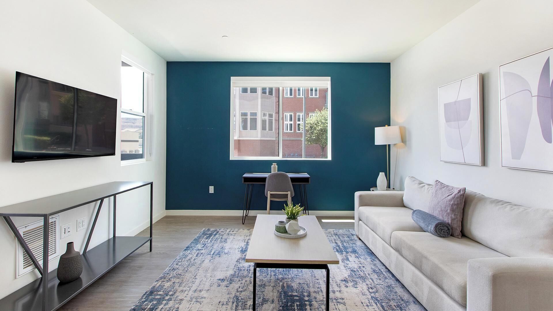 A modern living room with a large window, a flat-screen TV, a desk, and a sofa.