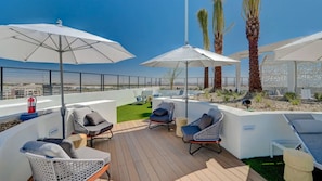 A rooftop terrace with outdoor seating, palm trees, and a clear view of the city skyline. - Landing | Amazing 2BD, Pool, Rooftop Lounge (Spring Valley)