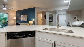 A modern kitchen with a dishwasher, white countertops, and a blue accent wall. - Landing | Chic 2BD, Gym, Pool (Orlando)