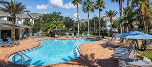A swimming pool with lounge chairs and umbrellas, surrounded by palm trees and buildings. - Landing | Chic 2BD, Gym, Pool (Orlando)