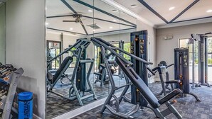 A gym with various exercise equipment, a mirror, and a wall-mounted TV. - Landing | Chic 2BD, Gym, Pool (Orlando)