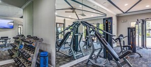 A gym with various exercise equipment, a mirror, and a wall-mounted TV. - Landing | Chic 2BD, Gym, Pool (Orlando)