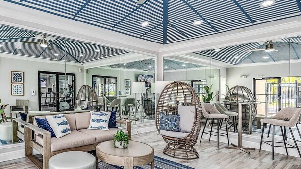A spacious living area with a high ceiling, wicker furniture, and a large plant. - Landing | Chic 2BD, Gym, Pool (Orlando)