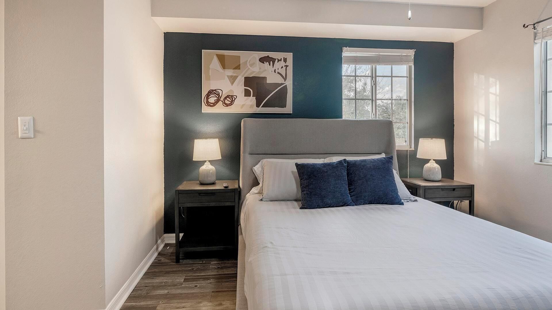 A bedroom with a bed, two nightstands, a window, and a wall art piece.