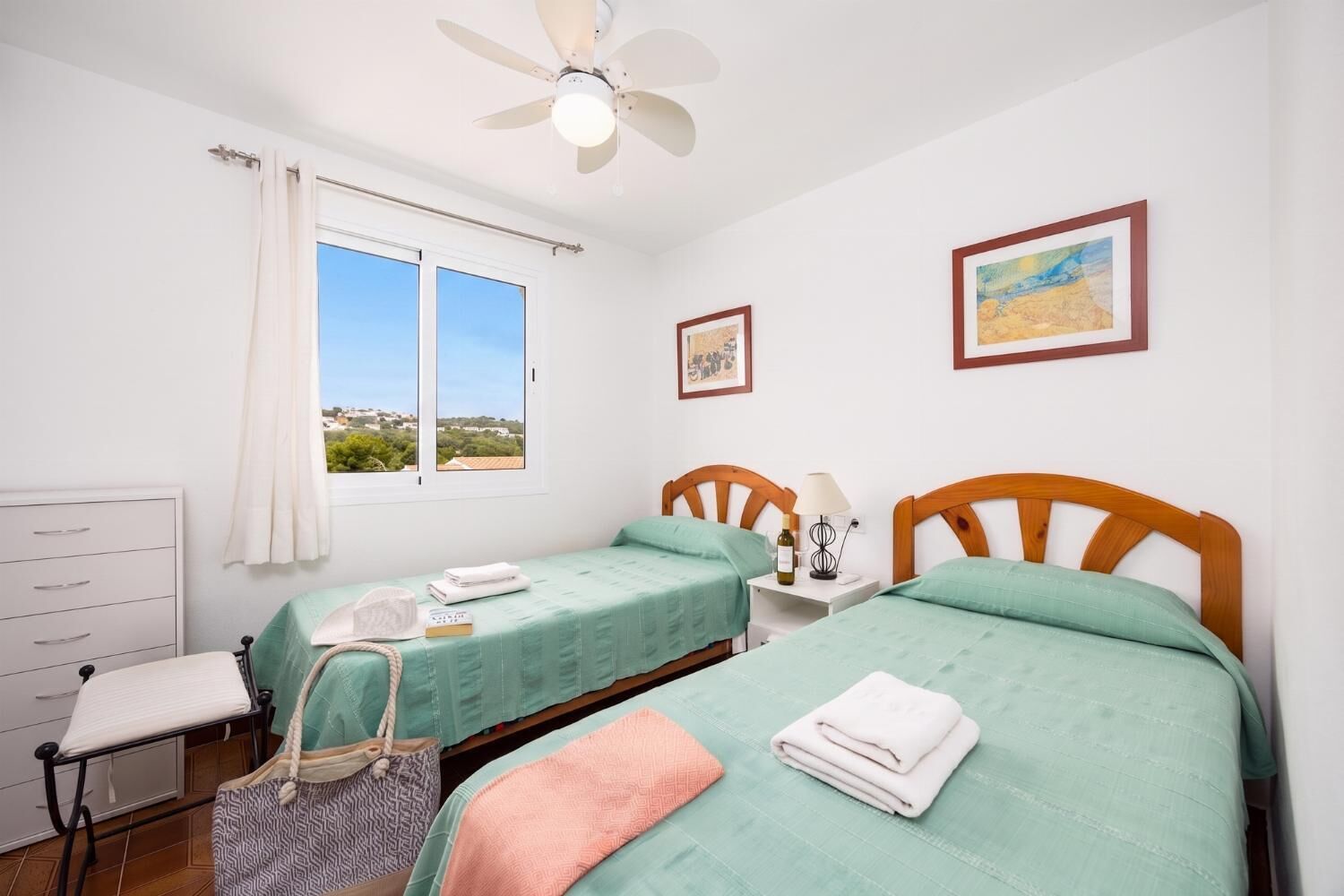Un dormitorio con dos camas, una ventana con vistas, un ventilador de techo y una mesita de noche con lámpara.