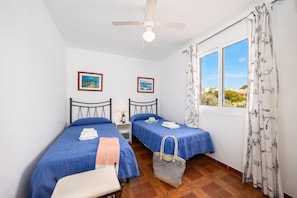 Une chambre avec deux lits, un ventilateur de plafond, une fenêtre avec des rideaux et une vue sur l’extérieur.